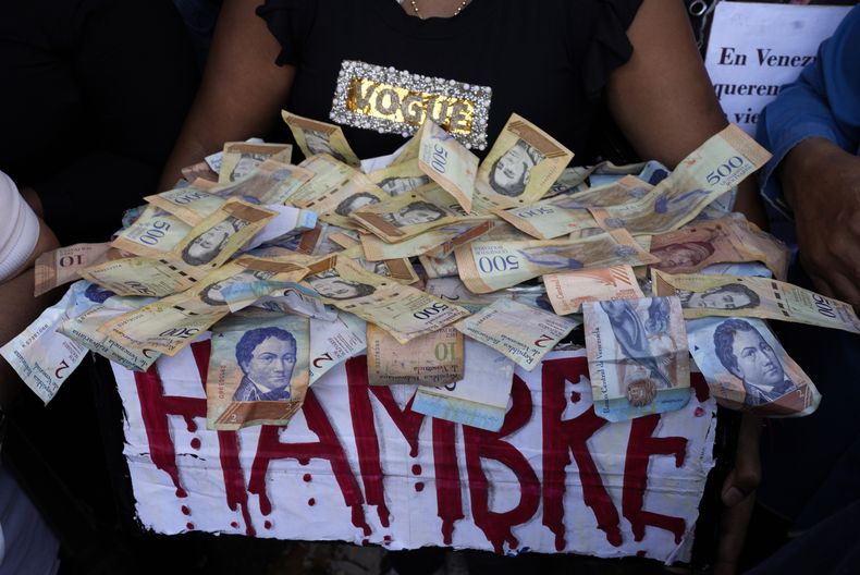 ARCHIVO - Un manifestante lleva una caja con la palabra hambre escrita en rojo y un montón de billetes de bolívares, en una protesta para reclamar mayores salarios y beneficios en Caracas, Venezuela, el 11 de enero de 2023. (AP Foto/Ariana Cubillos, Archivo)