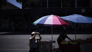 Una persona toma fotos del teatro chino mientras un vendedor callejero trabaja cerca de la sección de Hollywood en Los Ángeles, el martes 19 de agosto de 2025. (AP Foto/Jae C. Hong)