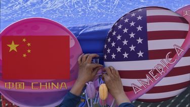 Un comerciante ata unas flores decoragivas entre dos banderas de China y Estados Unidos con forma de planeta, en una tienda durante el Carnaval de Primavera en Beijing, el 13 de mayo de 2023. (AP Foto/Andy Wong)