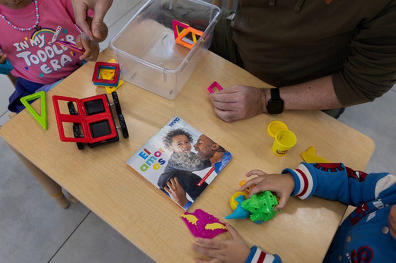 Una maestra y dos alumnos juegan con piezas de construcción magnéticas y pasta de modelar junto a un libro infantil titulado El amor es, en el John Cardinal OConnor Center for Parent and Child Development, un centro Head Start operado por The New York Foundling, en San Juan, Puerto Rico, el 13 de octubre de 2026. (AP Foto/Alejandro Granadillo)