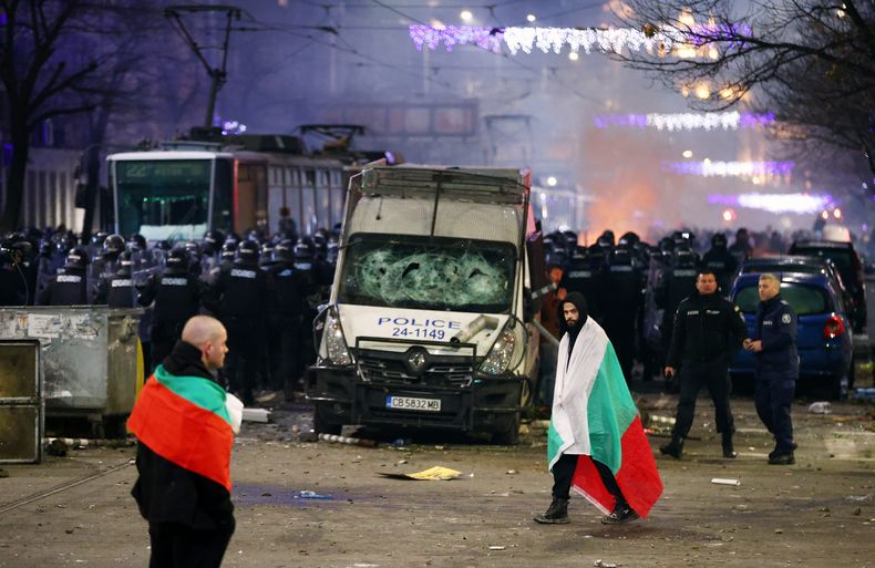 La policía se pone en formación mientras manifestantes caminan cubiertos por banderas nacionales durante una manifestación contra las medidas de austeridad que planea el gobierno de Bulgaria, en Sofía, 1 de diciembre de 2025. (Foto AP/Valentina Petrova)