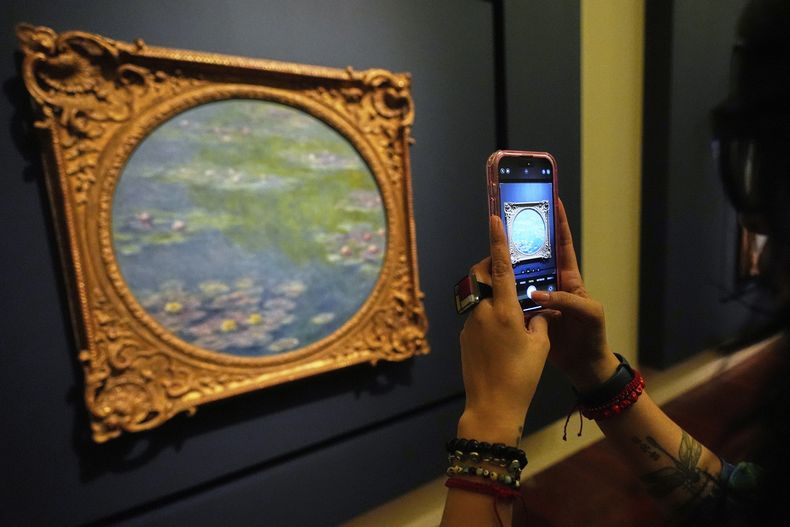 Un visitante toma fotografías de una pintura de Claude Monet durante una gira de prensa de la exposición: La Revolución Impresionista, en el Palacio de Bellas Artes en la Ciudad de México, el lunes 24 de marzo de 2025. (Foto AP/Fernando Llano)