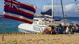 Turistas descienden de un bote de la empresa turística Trilogy Excursions, en la playa Kaanapali, junto a una bandera de Hawai colocada en la arena, el miércoles 6 de diciembre de 2023, en Lahaina, Hawai. (AP Foto/Lindsey Wasson)
