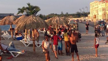 el malecon se convierte en una playa con arena, sombrillas y palmeras