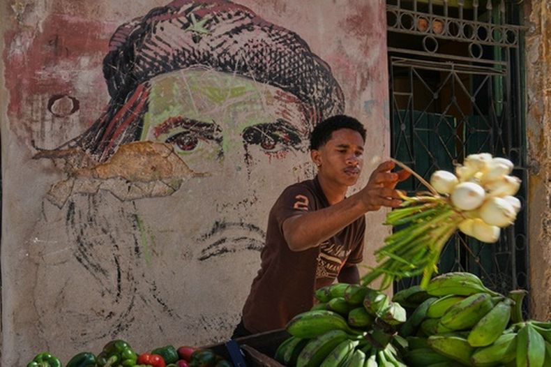 Un vendedor de verduras prepara cebollas para la venta en su carrito junto a un antiguo mural de Ernesto Che Guevara en La Habana Vieja, Cuba, el martes 6 de enero de 2026. (Foto AP/Ramon Espinosa)