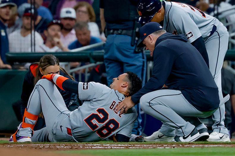 Javier Báez (28), de los Tigres de Detroit, es examinado por el mánager de los Tigres, A.J. Hinch (derecha), y un preparador físico del equipo tras lesionarse la pierna derecha mientras corría hacia la primera base en un rodado contra los Bravos de Atlanta, durante la quinta entrada de un partido de béisbol, el martes 28 de abril de 2026, en Atlanta. (AP Foto/Erik S. Lesser)