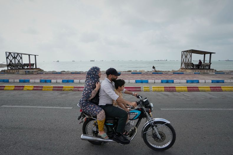 Un hombre, una mujer y un niño circulan en una motocicleta junto a la costa, mientras, de fondo, los buques comerciales esperan fondeados en el estrecho de Ormuz, ante la costa de Bandar Abbas, Irán, el 4 de septiembre de 2026. (AP Foto/Vahid Salemi)