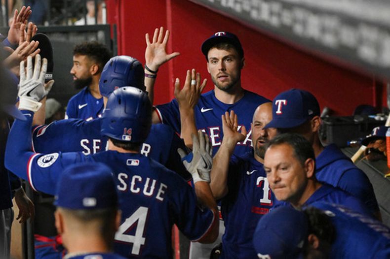 Justin Foscue (14) y Corey Seager, atrás, de los Rangers de Texas, son felicitados en su regreso al dugout después de anotar en la cuarta entrada del juego de béisbol de Grandes Ligas contra los Diamondbacks de Arizona el domingo 13 de septiembre de 2026, en Phoenix. (AP Foto/Caitlin OHara)