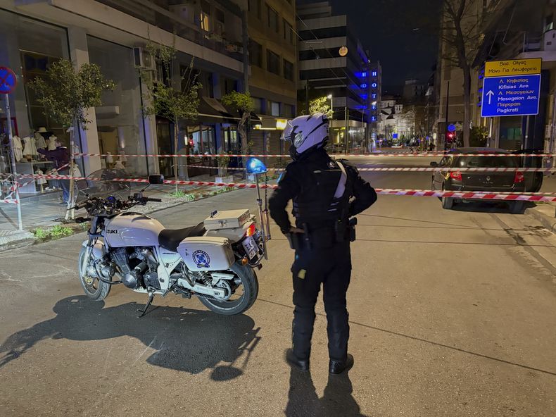 Un policía monta guardia tras la explosión de una presunta bomba fuera de las oficinas de Hellenic Train, la empresa que dirige el ferrocarril griego, el tercer edificio a la izquierda, en Atenas, Grecia, el viernes 11 de abril de 2025. (AP Foto/Derek Gatopoulos)