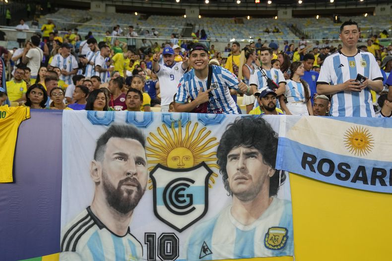 Hinchas alientan frente a una pancarta con la imagen del delantero argentino Lionel Messi y el fallecido astro Diego Maradona previo al partido entre Argentina y Brasil por las eliminatorias del Mundial, el martes 21 de noviembre de 2023, en Río de Janeiro (AP Foto/Silvia Izquierdo)