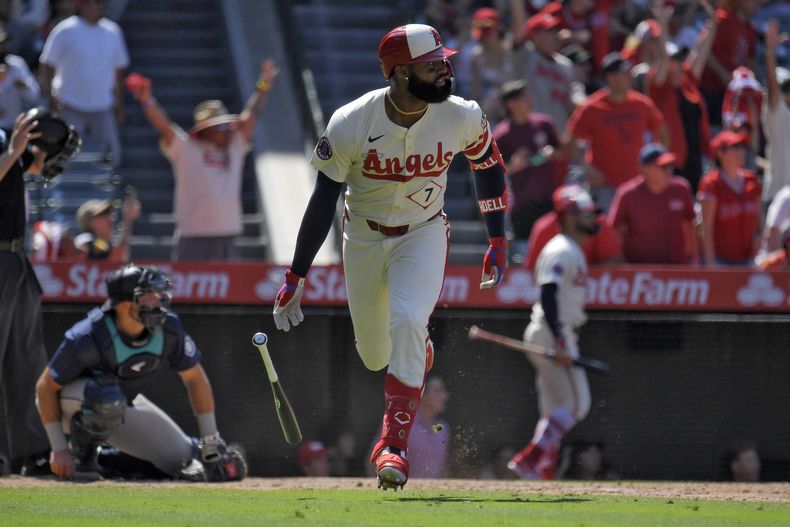 Jo Adell, de los Angelinos de Los Ángeles (derecha) observa su cuadrangular de tres carreras mientras el receptor de los Marineros de Seattle, Cal Raleigh pone rodilla sobre el plato durante el octavo episodio del juego de béisbol, el domingo 14 de julio de 2024, en Anaheim, California, EE.UU. (AP Foto/Mark J. Terrill)