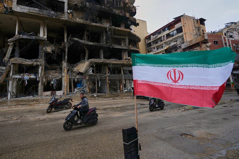 Un hombre en motoneta pasa cerca de una bandera iraní colocada frente a un edificio destruido tras un cese el fuego entre Hezbollah e Israel, en Dahiyeh, en los suburbios del sur de Beirut, Líbano, el lunes 20 de abril de 2026. (AP Foto/Hussein Malla)