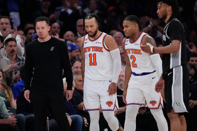 El base de los Knicks de Nueva York, Jalen Brunson (11), y el escolta Miles McBride (2) caminan hacia su banca mientras el entrenador en jefe de los Spurs de San Antonio, Mitch Johnson (izquierda), mira hacia otro lado durante la segunda mitad del Juego 3 de la serie de las Finales de la NBA, el lunes 8 de junio de 2026, en Nueva York. (Foto AP/Ross D. Franklin)