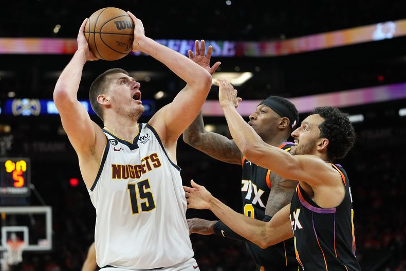 El serbio Nikola Jokic dispara por los Nuggets de Denver frente a Landry Shamet (derecha) y Torrey Craig, de los Suns de Phoenix, en el sexto duelo de la semifinal de la Conferencia Oeste, el jueves 11 de mayo de 2023 (AP Foto/Matt York)