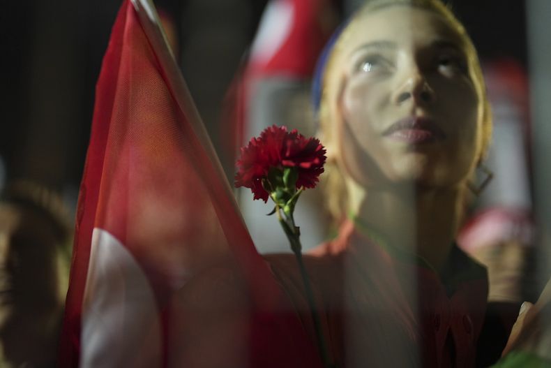Una manifestante sostiene una flor detrás de la barrera policial durante una protesta por el arresto del alcalde de Estambul, Ekrem Imamoglu, en Estambul, Turquía, el martes 25 de marzo de 2025. (AP Foto/Francisco Seco)