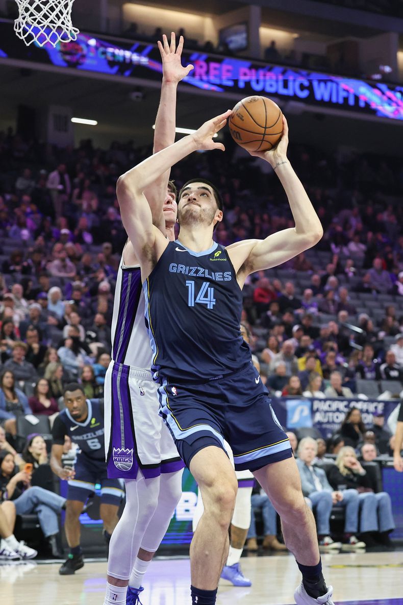 Zach Edey (14), de los Grizzlies de Memphis, se alza para dejar una bandeja con Maxime Raynaud, izquierda, defendiendo durante la primera mitad del juego de baloncesto de la NBA, el domingo 30 de noviembre de 2025, en Sacramento, California. (AP Foto/Sara Nevis)