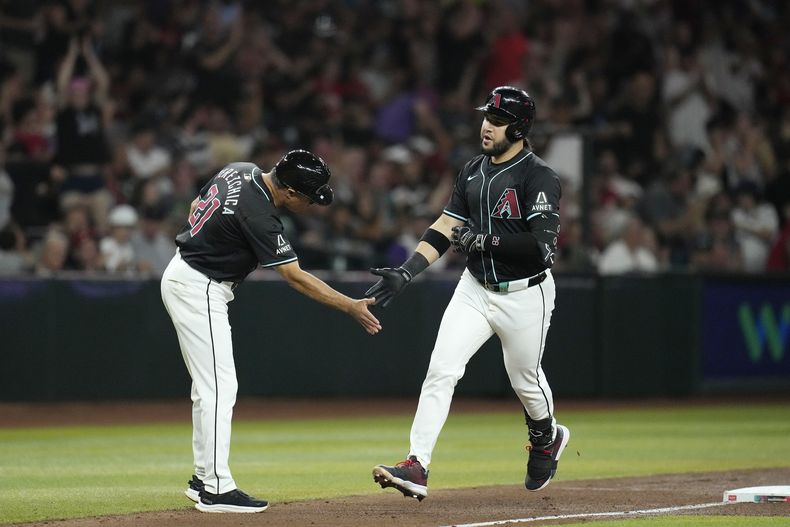 Eugenio Suárez, derecha, de los Diamondbacks de Arizona, celebra su cuadrangular en contra de los Medias Blancas de Chicago con el coach de tercera base Tony Perezchica, durante la cuarta entrada del juego de béisbol, el viernes 14 de junio de 2024, en Phoenix. (AP Foto/Ross D. Franklin)