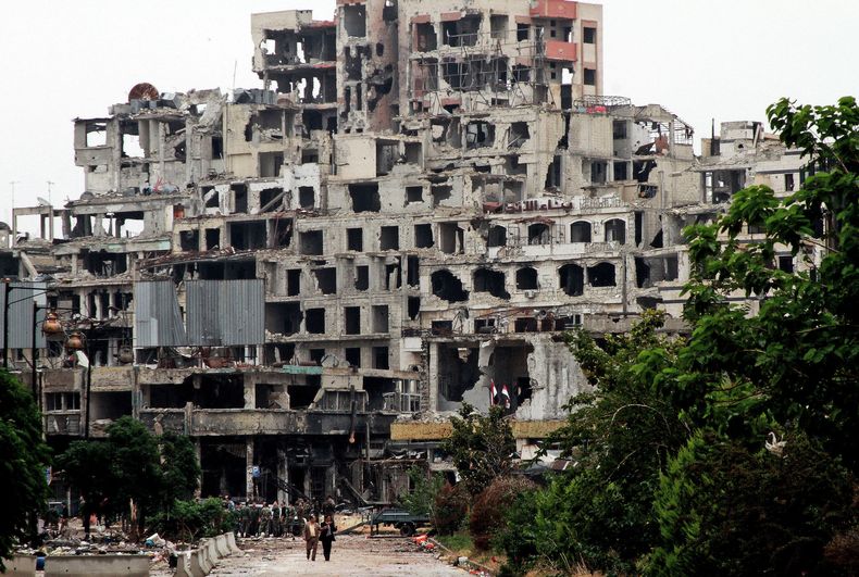 Funcionarios del gobierno sirio caminan por una calle frente a edificios da&ntilde;ados por los combates con insurgentes del Ej&eacute;rcito Libre Sirio en la ciudad vieja de Homs, Siria, 8 de mayo de 2014. Las fuerzas del gobierno sirio entraron a la ciu