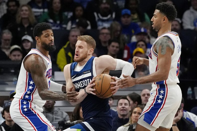 El escolta de los Timberwolves de Minnesota, Donte DiVincenzo, en el centro, conduce hacia la canasta entre el alero de los 76ers de Filadelfia, Paul George, a la izquierda, y el escolta Quentin Grimes, a la derecha, en el primer cuarto de un partido de baloncesto de la NBA, el martes 4 de marzo de 2025, en Minneapolis. (AP Foto/Bruce Kluckhohn)