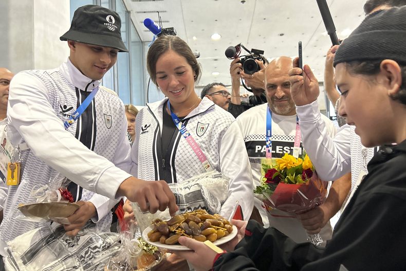 Los deportistas palestinos Yazan Al Bawwab y Valerie Tarazi toman dátiles ofrecidos por un niño a su llegada al aeropuerto de París, el jueves 25 de julio de 2024 (AP Foto/Megan Janetsky)