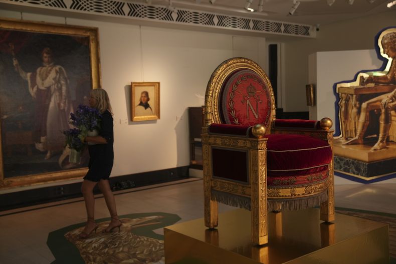 Una mujer camina junto a un trono en una exposición de pertenencias de Napoleón creada por el diseñador francés Jean-Charles de Castelbajac en la casa de subastas Sothebys en París el jueves 19 de junio de 2025 en París. (Foto AP/Christophe Ena)
