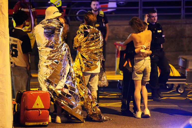 Dos personas se abrazan cerca de otras cubiertas con mantas térmicas, junto a personal de emergencias en Berlín, la madrugada del domingo 26 de julio de 2026 tras la cancelación de las celebraciones del Orgullo LGBTQ. (AP Foto/Markus Schreiber)