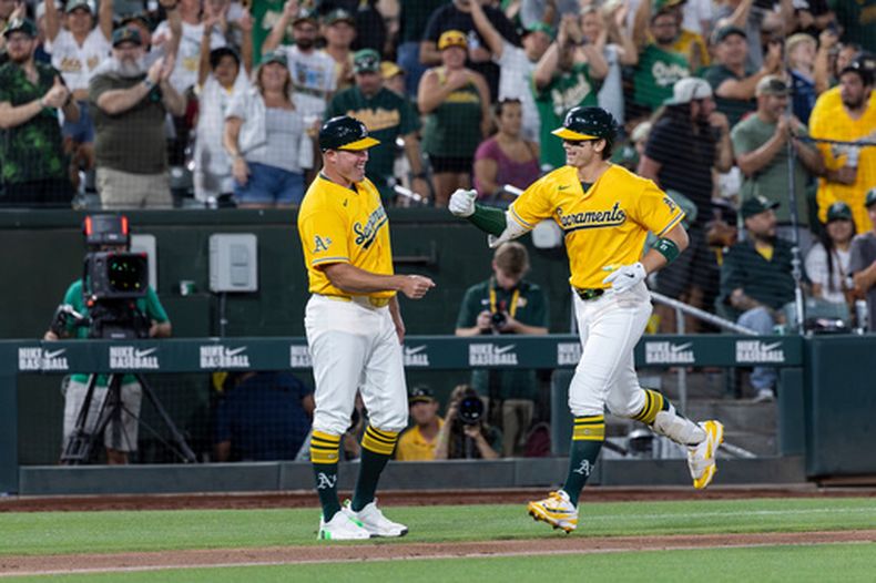 Tyler Soderstrom (derecha), de los Atléticos, choca los puños con el entrenador de tercera base Bobby Crosby tras conectar un jonrón de dos carreras durante la sexta entrada de un partido de béisbol contra los Nacionales de Washington, el sábado 18 de julio de 2026, en West Sacramento, California. (Foto AP/Sara Nevis)