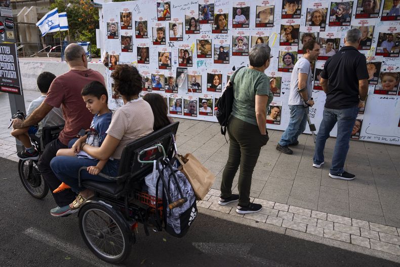 Varias personas observan fotografías de rehenes, en su mayoría civiles israelíes que fueron secuestrados durante el ataque del 7 de octubre de Hamás a Israel, el lunes 30 de octubre de 2023, en Tel Aviv, Israel. (AP Foto/Oded Balilty)
