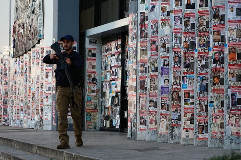 ARCHIVO - Un policía camina junto a carteles de personas desaparecidas ante la Fiscalía Especial en Personas Desaparecidas en Guadalajara, México, el 25 de febrero de 2026. (AP Foto/Marco Ugarte, Archivo)