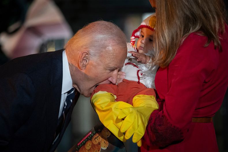 ARCHIVO - El presidente Joe Biden muerde, en broma, la pierna de un bebé al recibir, junto con su esposa Jill Biden, a estudiantes locales, niños vinculados con el Ejército, y familias vecinas antes de la celebración del Halloween, en el Jardín Sur de la Casa Blanca, en Washington, el 30 de octubre de 2024. (AP Foto/Ben Curtis)
