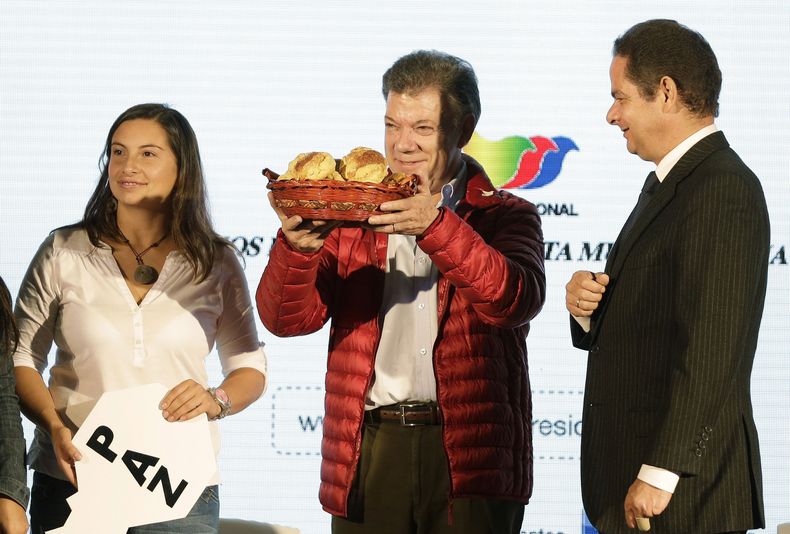 El presidente colombiano Juan Manuel Santos muestra una canasta con pan que le regal&oacute; una simpatizante, izquierda, durante un mitin de campa&ntilde;a en Soacha, en las afueras de Bogot&aacute;, Colombia, el lunes 12 de mayo de 2014. A la derecha es