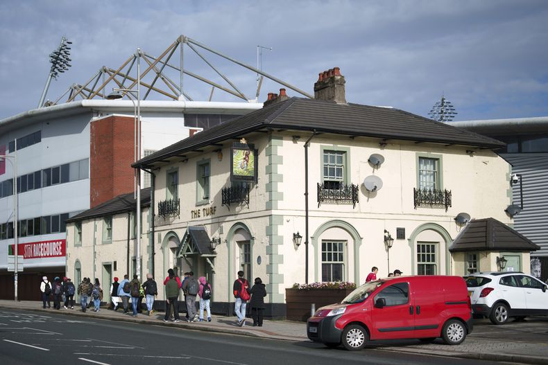 Personas caminan frente al pub The Turf junto al hipódromo del Wrexham Football Club en Wrexham, Gales, el lunes 7 de octubre de 2024. (Foto AP/Jon Super)