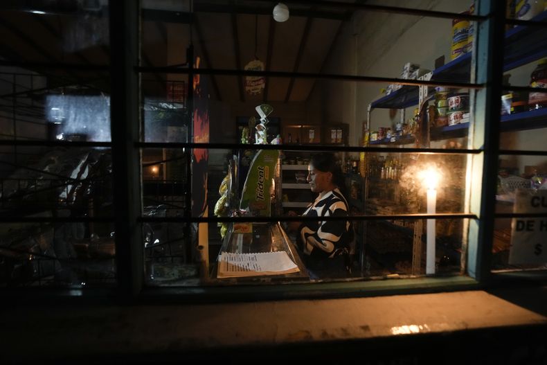 Mónica Valiente espera que lleguen clientes en su panadería, iluminada con una vela, durante un apagón eléctrico por racionamiento en Quito, Ecuador, el martes 15 de octubre de 2024. (AP Foto/Dolores Ochoa)