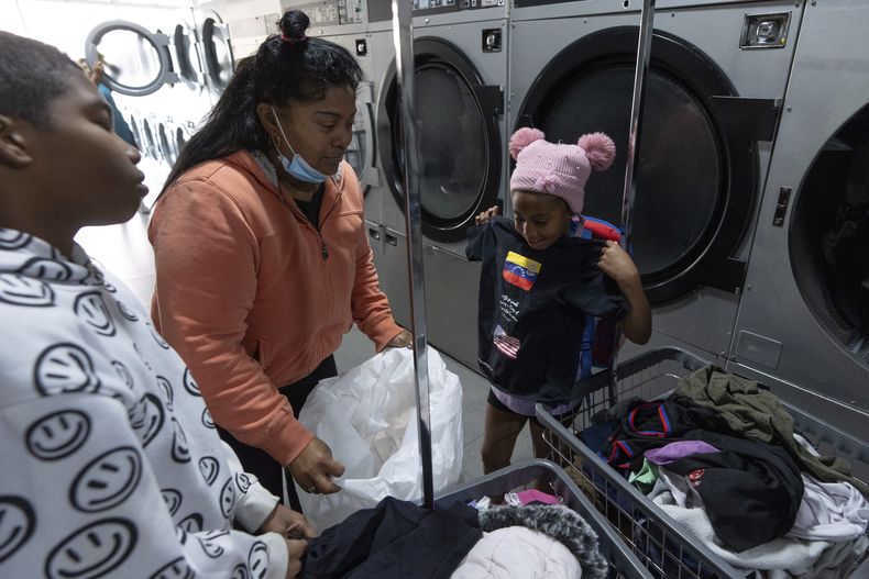 Margelis Rodríguez, de Venezuela, en el centro, mira a su hija de 6 años, Maickeliys, sosteniendo una camiseta con las banderas de Venezuela y Estados Unidos y el mensaje en español Sí se pudo gracias a Dios el tiempo valió la pena lo logré!!, en una lavandería cerca del refugio para migrantes donde se alojan en Tijuana, México, el viernes 31 de enero de 2025. (AP Foto/Gregory Bull)