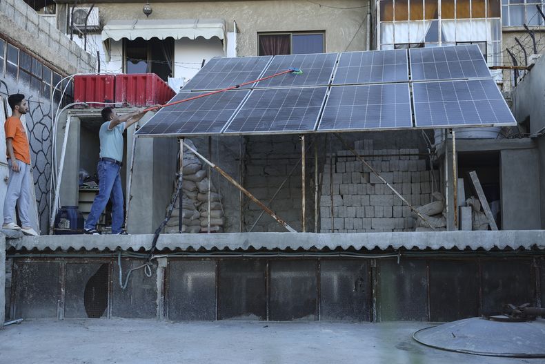 El sirio Abdul Razzaq Al Jenan limpia páneles solares ubicados en el techo de su casa, el domingo 29 de junio de 2025, en Damasco, Siria. (AP Foto/Ghaith Alsayed)