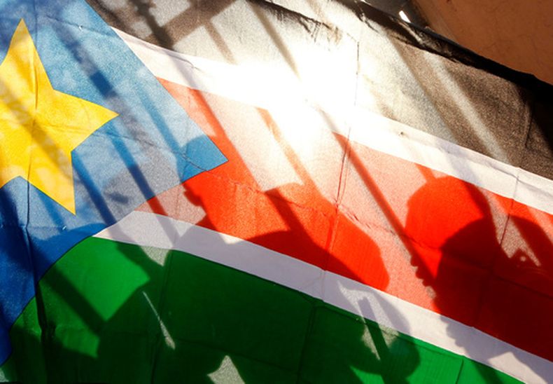 ARCHIVO – Las siluetas de habitantes de Sudán del Sur vistas a través de una bandera de ese país mientras forman una fila para votar en Juba, Sudán del Sur, el 9 de enero de 2011. (AP Foto/Jerome Delay, Archivo)