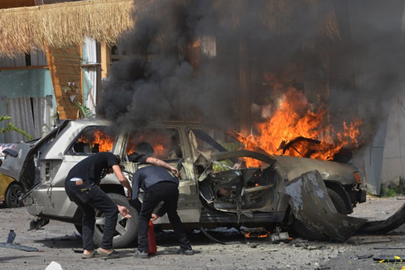 Una persona se ve en un vehículo en llamas mientras hombres intentan apagar el fuego tras un ataque israelí conta un auto en la localidad costera de Barja, en el sur de Beirut, Líbano, el miércoles 13 de mayo de 2026. (AP Foto/Mustafa Jamalddine)