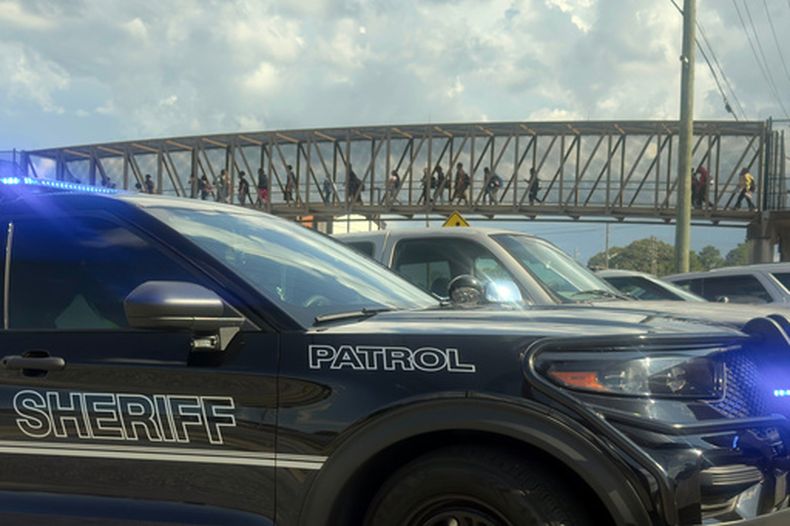 Estudiantes salen de la Escuela Secundaria Warner Robins, mientras vehículos del Departamento de Policía del condado de Houston aguardan en el lugar después de un tiroteo en la escuela, el miércoles 12 de agosto de 2026, en Warner Robins, Georgia. (Joe Kovac/Atlanta Journal-Constitution via AP)