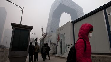 americateve | Una mujer cubierta con una mascarilla para frente a un cartel, centro, que proclama "China, adelante", en el distrito comercial central de Beijing el jueves, 20 de febrero del 2014. (Foto AP/Alexander F. Yuan)