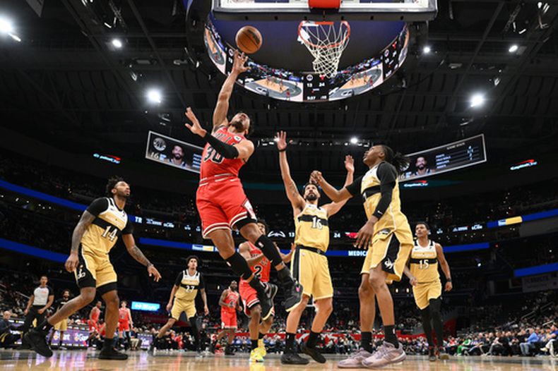 Tre Jones, base de los Bulls de Chicago, encesta frente a Anthony Gill (16), Leaky Black (14), Bub Carrington (7) y Juju Reese (15) en el duelo ante los Wizards de Washington, el jueves 9 de abril de 2026 (AP Foto/Nick Wass)