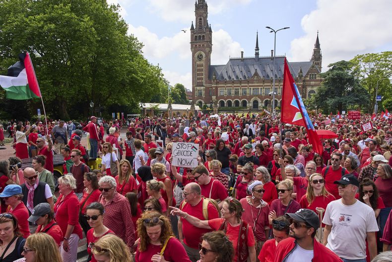 Decenas de miles de personas vestidas de rojo marchan frente al Palacio de la Paz, sede de la Corte Internacional de Justicia, al fondo, para exigir que su gobierno haga más para frenar la campaña militar de Israel en la Franja de Gaza, el domingo 15 de junio de 2025, en La Haya, Holanda. (AP Foto/Peter Dejong)