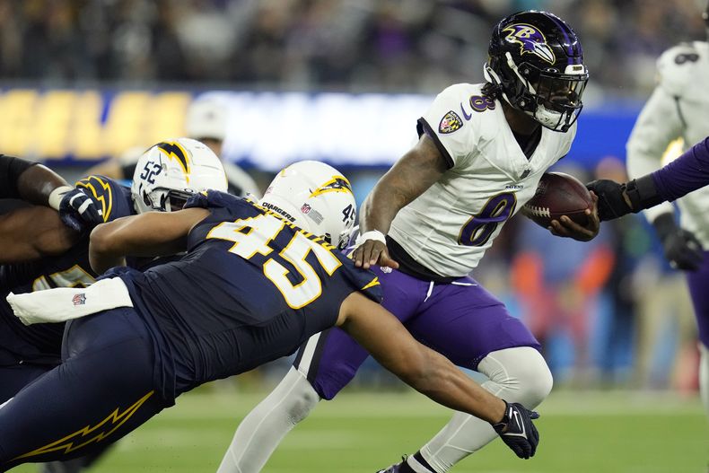 Lamar Jackson (8), quarterback de los Ravens de Baltimore, corre para escapar de la presión de los linebackers de los Chargers de Los Ángeles, Khalil Mack (52) y Tuli Tuipulotu (45) durante la primera mitad del juego de la NFL, el domingo 26 de noviembre de 2023, en Inglewood, California. (AP Foto/Ashley Landis)
