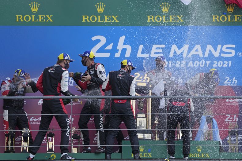 ARCHIVO - Los pilotos ganadores del equipo Toyota Gazoo Racing, el británico Mike Conway, el japones Kamui Kobayashi y el argentino José María López, y los del segundo lugar, el suizo Sebastien Buemi, el japónes Kazuki Nakajima y el neocelandés Brendon Hartley, festejan en el podio al término de la carrera de resistencia de las 24 horas de Le Mans, en Francia, el 22 de agosto de 2021. (AP Foto/Francois Mori, Archivo)