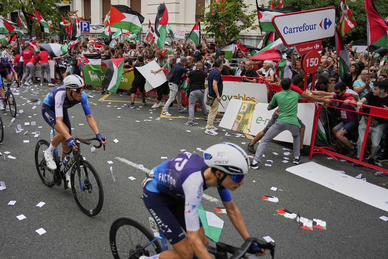 Ciclistas del equipo Israel Premier Tech compiten en la Vuelta a España mientras manifestantes protestan con banderas palestinas durante la 11ma etapa, el miércoles 3 de septiembre de 2025. (AP Foto/Miguel Oses)