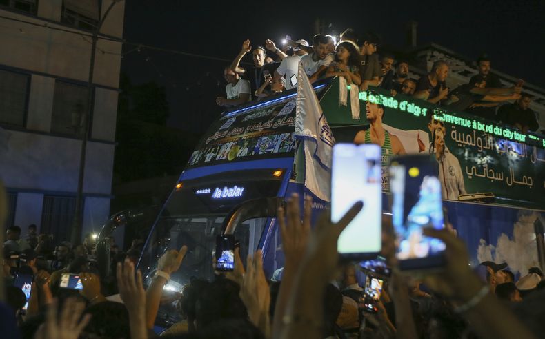 Imane Khelif, campeona olímpica de boxeo, saluda a la multitud desde un autobús, al desfilar por Tiaret, Argelia, el viernes 16 de agosto de 2024 (AP Foto/Anis Belghoul)