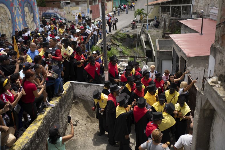 Devotos, vestidos con ropas coloniales y pañuelos que representan los colores de partidos políticos de esa época y con las caras pintadas de negro, participan en la popular fiesta de la Parranda de San Pedro en Guatire, Venezuela, el jueves 29 de junio de 2023. (AP Foto/Ariana Cubillos)