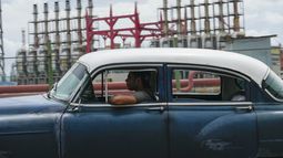 Una persona conduce un automóvil clásico estadounidense junto a un generador flotante que no produce electricidad desde hace días en La Habana, Cuba, el viernes 18 de octubre de 2024. (AP Foto/Ramón Espinosa)