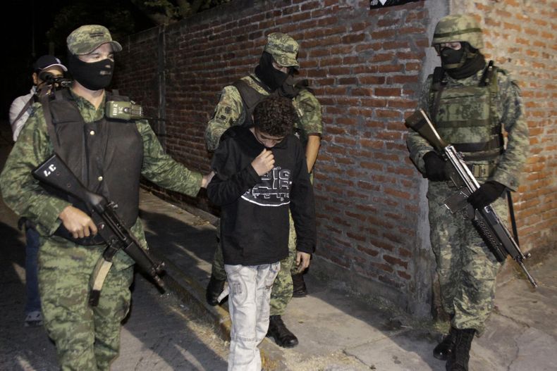 ARCHIVO - La foto del 3 de diciembre de 2010 muestra a soldados mexicanos que custodian a Edgar, conocido como  "El Ponchis" y el "ni&ntilde;o sicario", quien confeso haber perpetrado asesinatos  para el cartel de los hermanos Beltr&aa