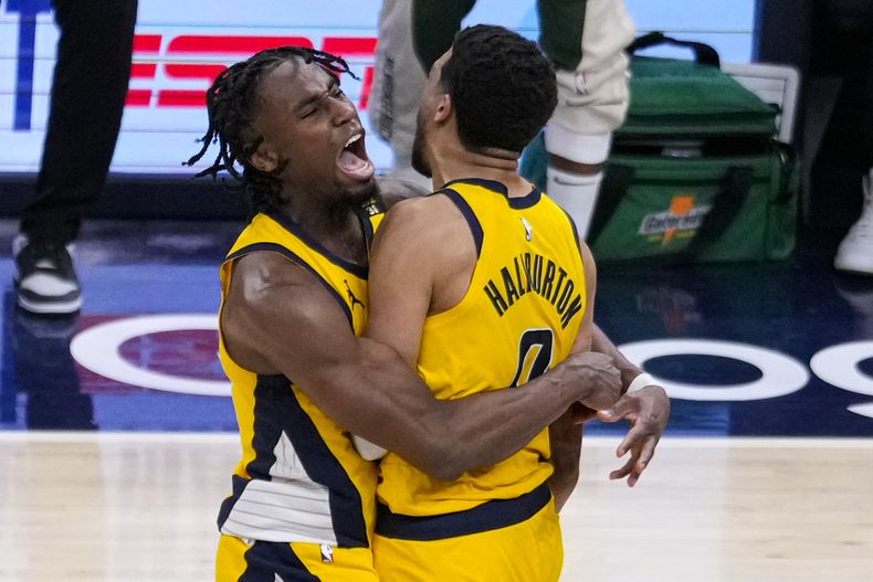 El armador de los Pacers de Indiana Tyrese Haliburton (0) es abrazado por su compañero el alero Aaron Nesmith (23) luego de atinar el tiro ganador durante la prórroga en el 2do juego de la ronda de la primera ronda playoffs de la NBA, el viernes 26 de abril de 2024, en Indianápolis.(AP Foto/Michael Conroy)