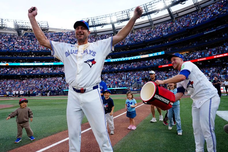 Max Scherzer, de los Azulejos de Toronto, reacciona mientras sus hijos observan a su compañero Myles Straw, derecha, arrojarle un balde de agua, celebrando la trayectoria despues del partido de béisbol de Grandes Ligas ante los Rojos de Cincinnati, el domingo 27 de septiembre de 2026, en Toronto. (Frank Gunn/The Canadian Press via AP)